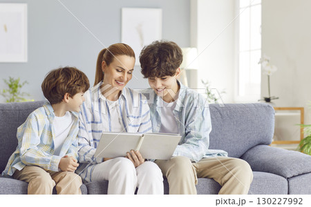 Loving family mother, caring woman with little and teen son watching pictures in photo album 130227992