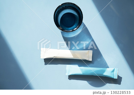 White and blue collagen supplement sticks with glass of water. White and blue collagen supplement sticks with glass of water. 130228533