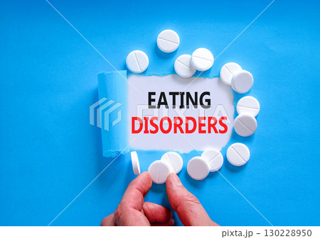 Eating disorders symbol. Concept words Eating disorders on beautiful white paper. White pills tablets. Doctor's hand. Beautiful blue background. Medical healthy lifestyle eating disorders concept. 130228950