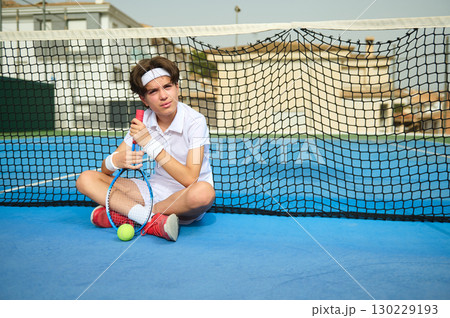 Young Tennis Player Resting by Net on Outdoor Court 130229193