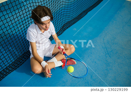 Young Tennis Player Resting on the Court Near the Net in Contemplation Young Tennis Player Resting on the Court Near the Net in Contemplation 130229199
