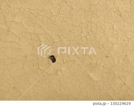 Close up of cracked beige paint with a small hole in the center surface 130229629