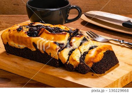 Blueberry cheese brownie with a metal fork and black ceramic coffee cup on wooden cutting board. 130229668