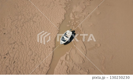 Aerial view of a stranded boat on cracked dry land near a small body of water 130230230