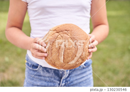 Female caucasian teen holding fresh round bread outdoors in casual white shirt 130230546