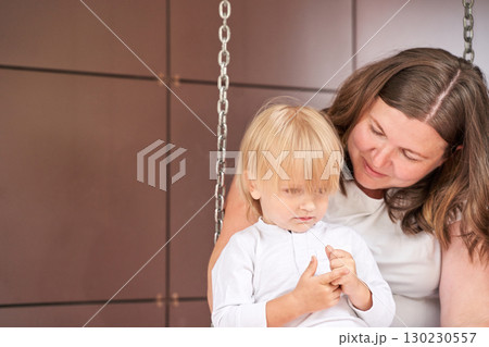 Caucasian female adult and young child bonding on swing in warm indoor setting 130230557
