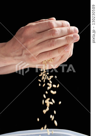 Caucasian adult hands holding and pouring rice grains against black background Caucasian adult hands holding and pouring rice grains against black background 130230589
