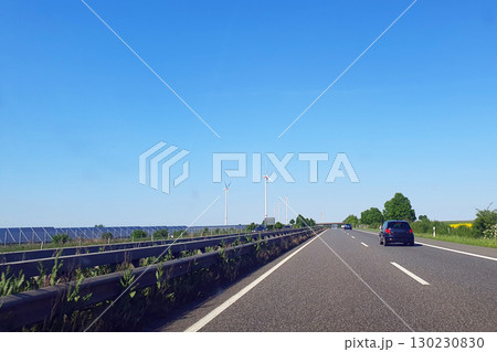 Cars drive on the highway with much windmills. Nature background with green field, trees and blue sky. Wind turbines for alternative green energy in Europe. Cars drive on the highway with much windmills. Nature background with green field, trees and blue sky. Wind turbines for alternative green energy in Europe. 130230830