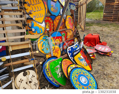 A collection of colorful shields and swords are displayed in a field. 130231038
