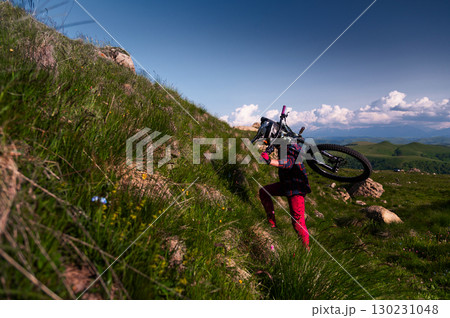 Male athlete cyclist carries his mountain bike uphill. Summer downhill mtb bike concept 130231048