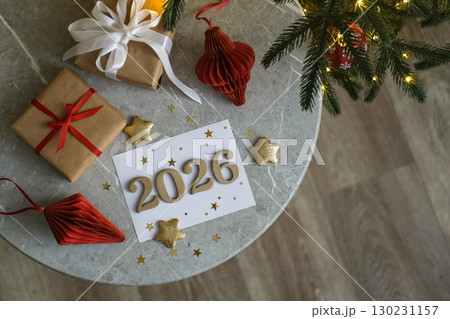 Top view of round table with greeting card with gold numbers 2026, stars, gifts and holiday decorations. Perfect for celebrating the New Year Top view of round table with greeting card with gold numbers 2026, stars, gifts and holiday decorations. Perfect for celebrating the New Year 130231157