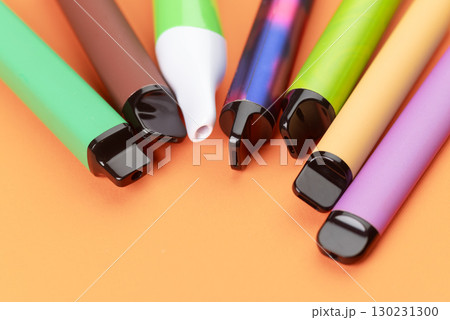 Colorful disposable vape pens on orange background, modern electronic smoking devices closeup. Colorful disposable vape pens on orange background, modern electronic smoking devices closeup. 130231300