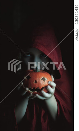 Child in red cloak holding carved pumpkin at night 130231436