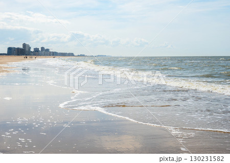 People walking on the sand beach near the sea with a lot of houses and hotel in the evening. Sand, relax and sunset in Ostend, Belgium. People walking on the sand beach near the sea with a lot of houses and hotel in the evening. Sand, relax and sunset in Ostend, Belgium. 130231582
