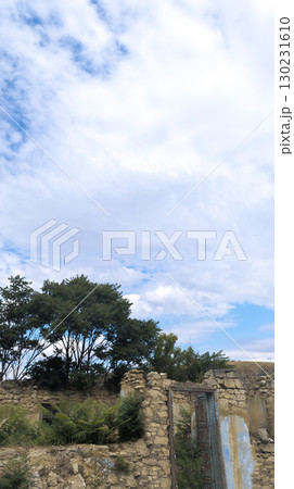 Crumbling stone wall with rusty metal door frame standing beneath cloudy blue sky Crumbling stone wall with rusty metal door frame standing beneath cloudy blue sky 130231610