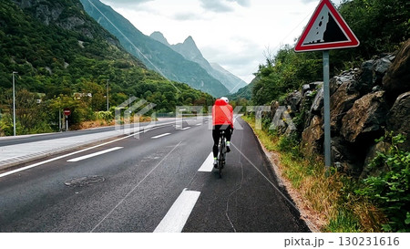 Cyclist riding on a mountain road with dramatic peaks of Belledonne in the background. Following camera view in the French Alps 130231616