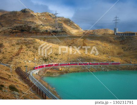 Aerial view of red train near alpine mountain lake and cloudy sky 130231791