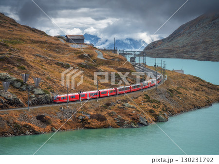 Aerial view of red train near alpine mountain lake and cloudy sky 130231792