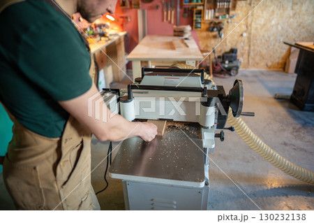 Skilled craftsman working with wood on planer thicknesser jointer, preparing furniture materials Skilled craftsman working with wood on planer thicknesser jointer, preparing furniture materials 130232138