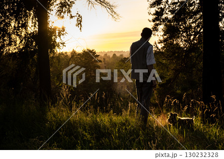 man walks with dog through field during sunset in peaceful forest setting. closeup. man walks with dog through field during sunset in peaceful forest setting. closeup. 130232328