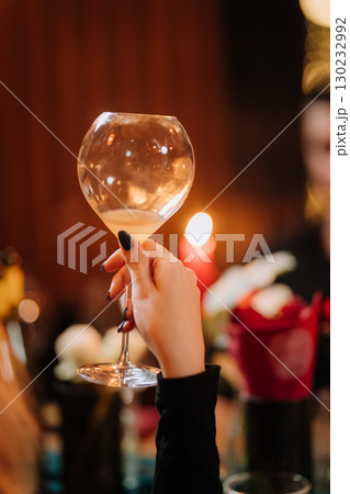 Elegant hand holding wine glass at cozy candlelit dinner with floral decor Elegant hand holding wine glass at cozy candlelit dinner with floral decor 130232992