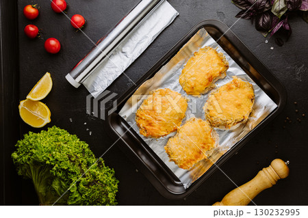 Baked chicken fillets with melted cheese on foil in a tray, top view, rustic background 130232995