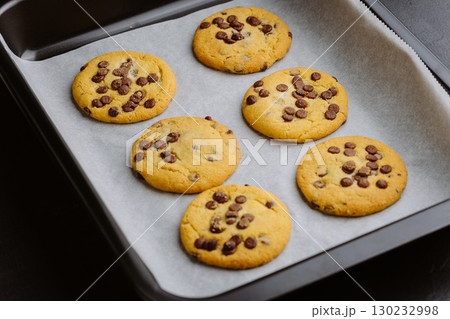 Freshly baked chocolate chip cookies on a baking tray with parchment paper 130232998
