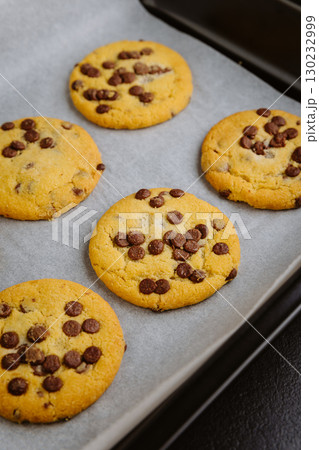 Freshly baked chocolate chip cookies in tray on parchment paper, closeup food photography 130232999