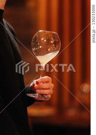 Hand holding elegant wine glass with cloudy white beverage, warm ambient lighting 130233000