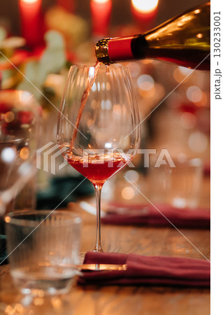 Pouring rose wine into glass at festive dinner with flowers and candlelight ambiance 130233001