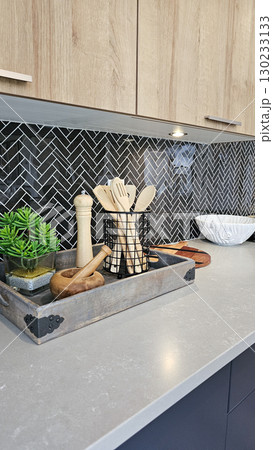 Modern kitchen countertop featuring stylish utensils in a decorative tray, with herringbone backsplash and natural elements enhancing the culinary space Modern kitchen countertop featuring stylish utensils in a decorative tray, with herringbone backsplash and natural elements enhancing the culinary space 130233133