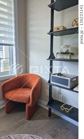 Cozy orange chair positioned beside modern shelving unit with decorative items, creating a stylish and inviting interior space 130233141