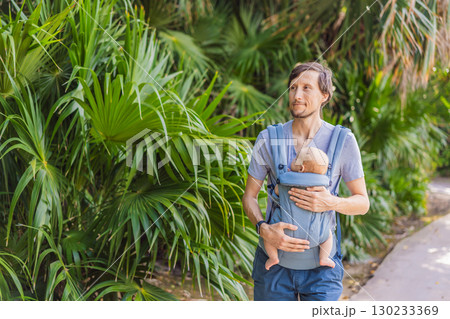 Young father walks in nature with his baby son nestled close in a parent-facing ergonomic baby carrier. Bonding, warmth, and modern parenting concept in a peaceful outdoor setting 130233369