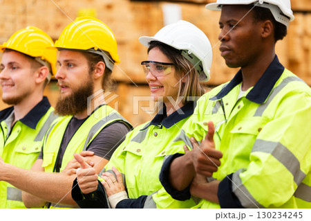 Confident warehouse workers in high visibility safety gear with crossed arms, standing in lumber storage facility, representing unity, professionalism, and industrial team motivation. Confident warehouse workers in high visibility safety gear with crossed arms, standing in lumber storage facility, representing unity, professionalism, and industrial team motivation. 130234245