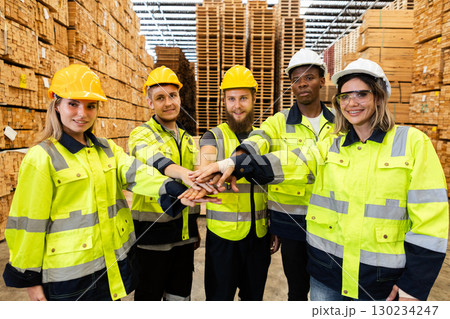 Diverse warehouse workers in reflective safety jackets joining hands in teamwork gesture inside a lumber storage facility, symbolizing unity, collaboration, and industrial motivation. Diverse warehouse workers in reflective safety jackets joining hands in teamwork gesture inside a lumber storage facility, symbolizing unity, collaboration, and industrial motivation. 130234247
