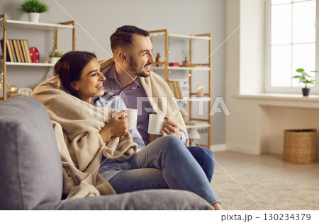 Loving affectionate couple sitting in modern living room wrapped with warm blanket, happy romantic  130234379