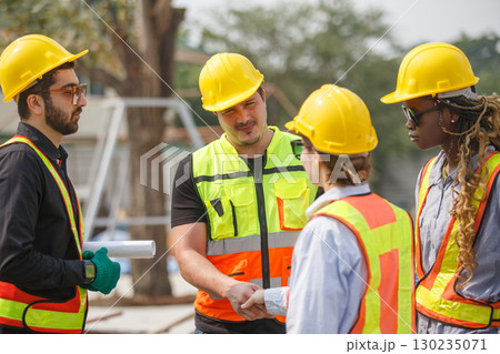 Diverse construction team wearing safety helmets and reflective vests shaking hands at building site symbolizing teamwork, agreement, partnership and successful project collaboration. 130235071