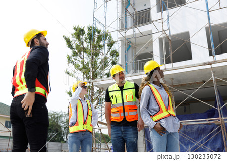 Group of diverse construction workers wearing safety helmets and reflective vests inspecting building site progress, representing teamwork, engineering, safety, and project development planning. Group of diverse construction workers wearing safety helmets and reflective vests inspecting building site progress, representing teamwork, engineering, safety, and project development planning. 130235072