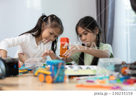 Two asian girls work together on a colorful STEM robotics project, focusing on assembling parts to develop creativity, engineering skills, and problem-solving through hands-on learning. 130235159