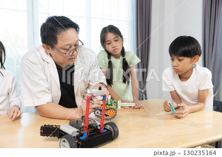 Teacher guiding diverse children in STEM robotics class, encouraging teamwork and creativity while building and programming toy robots in an education, inspiring classroom environment. 130235164