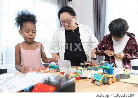 Teacher guides diverse students building colorful STEM robotics projects, encouraging creativity, engineering skills, and teamwork through engaging hands-on learning activities. 130235184