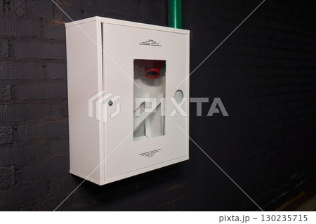 A White Emergency Fire Equipment Cabinet mounted on a Black Wall within a facility setting 130235715