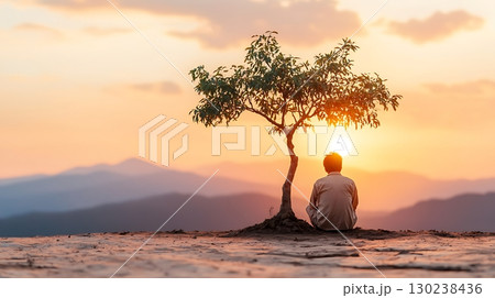 Person Sitting Near a Tree Under a Beautiful Sunset with Mountains in the Background 130238436