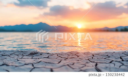 Beautiful Sunset Over Water with Cracked Earth and Mountain Silhouette in Background 130238442