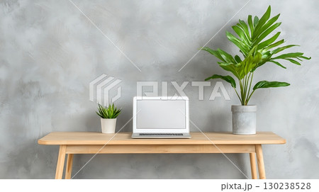 Minimalist Workspace with Laptop and Green Plant on Wooden Desk Against Gray Wall 130238528