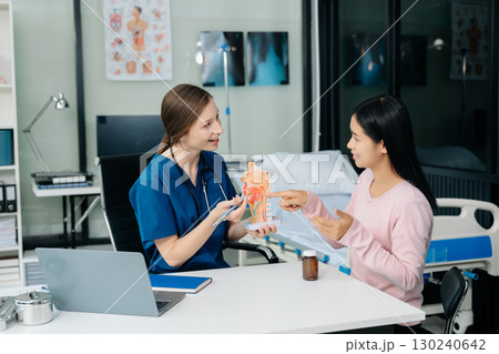 Doctor discussing treatment with Female patient talks to discuss results or symptoms and sitting on examination desk 130240642