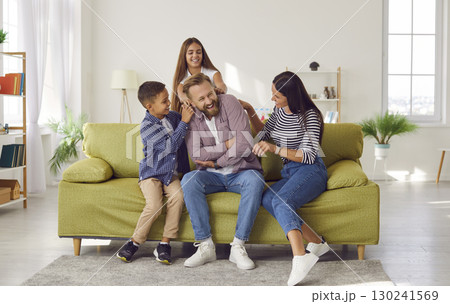 Happy laughing kids boy and girl having fun with their parents, sitting on sofa at home. 130241569