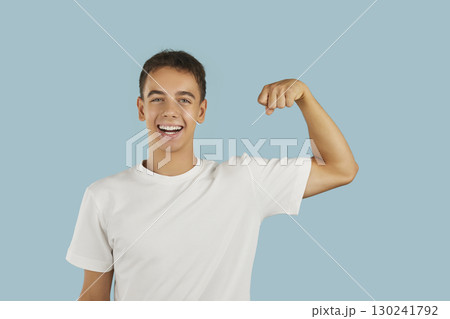 Young smiling boy celebrate victory with hand in fist demonstrating strength on blue background. Young smiling boy celebrate victory with hand in fist demonstrating strength on blue background. 130241792