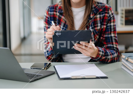 Beautiful woman using laptop and tablet while sitting at her working place. Concentrated Beautiful woman using laptop and tablet while sitting at her working place. Concentrated 130242637