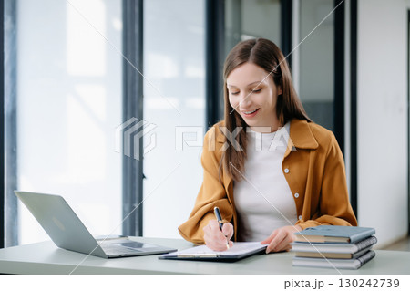 Confident woman with a smile standing holding notepad and tablet at the office. Confident woman with a smile standing holding notepad and tablet at the office. 130242739